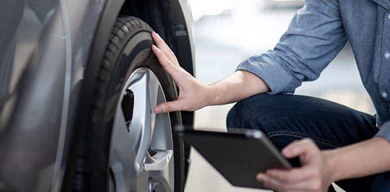 Man with ipad inspecting tire on car